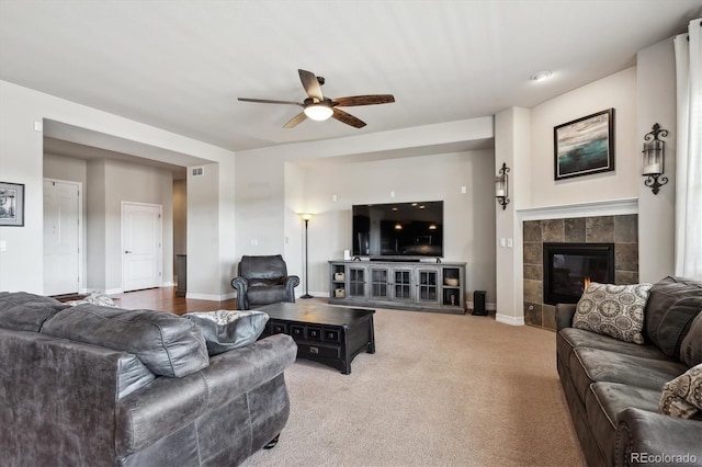 living area with visible vents, baseboards, a tiled fireplace, carpet flooring, and a ceiling fan