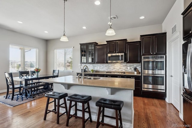 kitchen featuring visible vents, stainless steel appliances, a sink, a kitchen breakfast bar, and backsplash