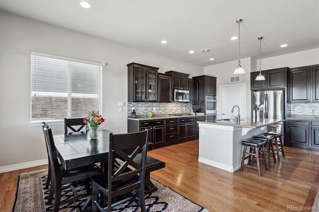 kitchen featuring a sink, a kitchen bar, light wood-style flooring, stainless steel appliances, and a kitchen island with sink