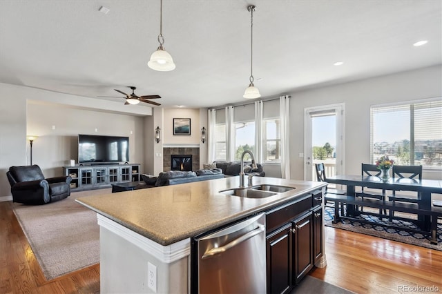 kitchen featuring a tiled fireplace, dishwasher, an island with sink, wood finished floors, and a sink