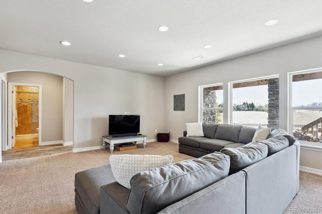 living area featuring light colored carpet, arched walkways, and baseboards