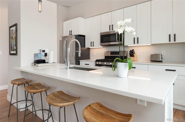 kitchen featuring white cabinetry, backsplash, wood-type flooring, a kitchen bar, and appliances with stainless steel finishes