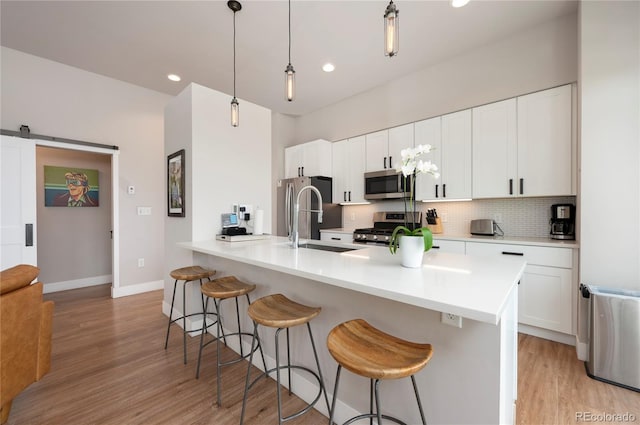 kitchen with pendant lighting, white cabinets, light hardwood / wood-style flooring, a barn door, and appliances with stainless steel finishes