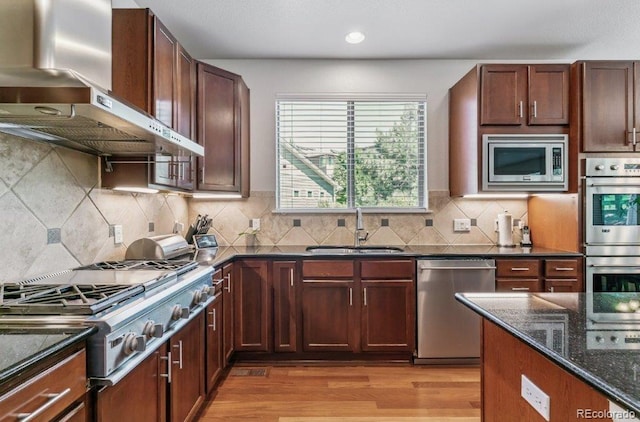 25402 E Glasgow Pl, Aurora, CO 80016 - kitchen featuring wall chimney range hood, stainless steel appliances, dark stone countertops, light wood finished floors, and backsplash