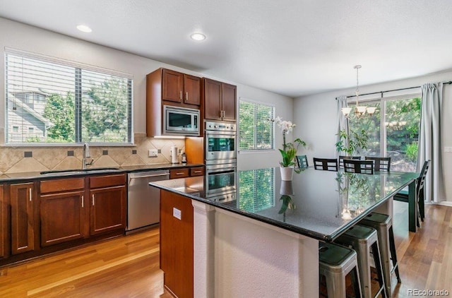 25402 E Glasgow Pl, Aurora, CO 80016 - kitchen featuring stainless steel appliances, light wood finished floors, a chandelier, a kitchen island, and backsplash