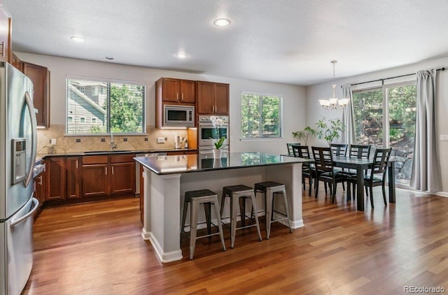 25402 E Glasgow Pl, Aurora, CO 80016 - kitchen featuring stainless steel appliances, a chandelier, dark countertops, a kitchen breakfast bar, and wood finished floors