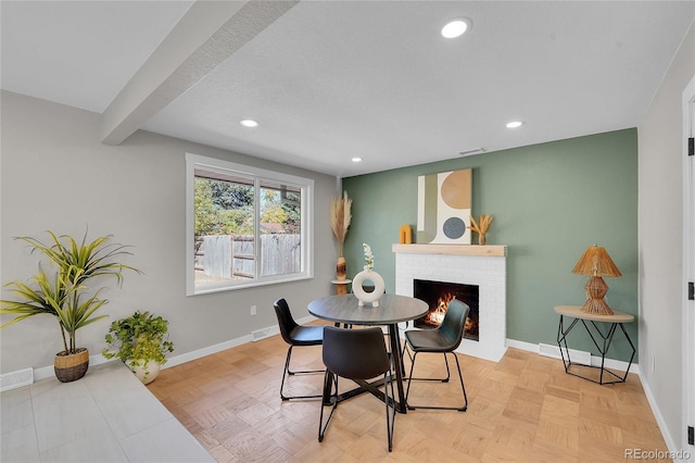 dining room featuring a brick fireplace, beam ceiling, and light parquet flooring