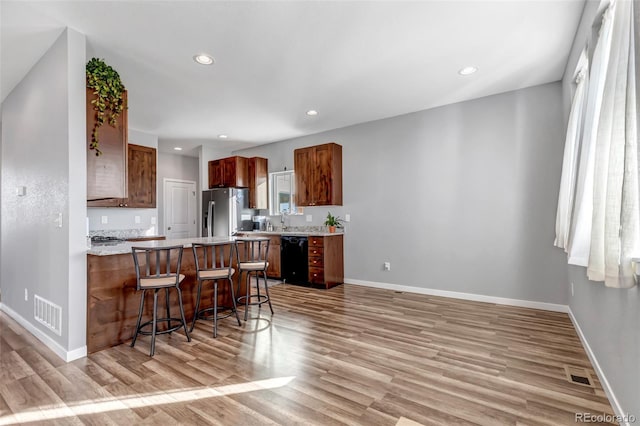 kitchen with stainless steel refrigerator with ice dispenser, a kitchen breakfast bar, light hardwood / wood-style floors, and dishwasher