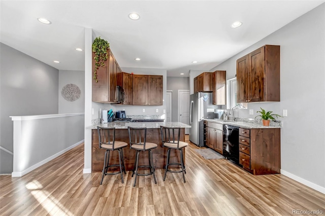 kitchen featuring sink, stainless steel appliances, light stone counters, a breakfast bar area, and light wood-type flooring