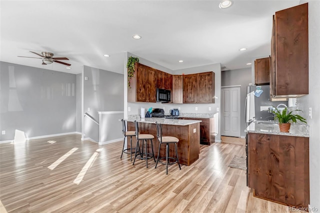 kitchen featuring ceiling fan, a center island, stove, a breakfast bar area, and light wood-type flooring