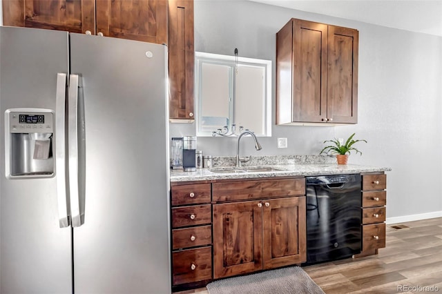 kitchen featuring dishwasher, sink, stainless steel fridge, light stone countertops, and light hardwood / wood-style floors