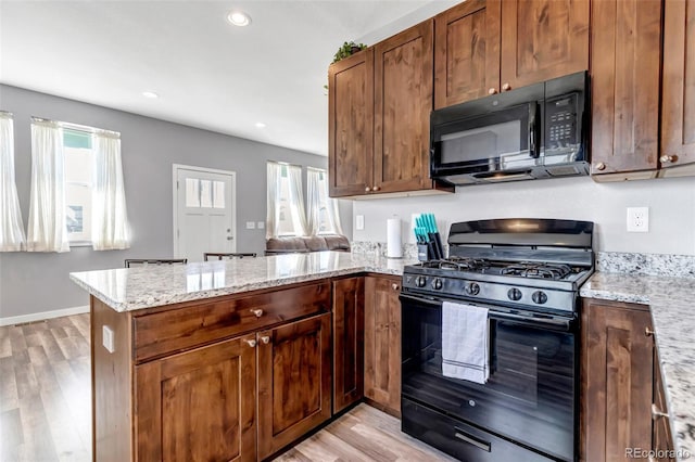 kitchen featuring kitchen peninsula, light hardwood / wood-style floors, light stone counters, and black appliances