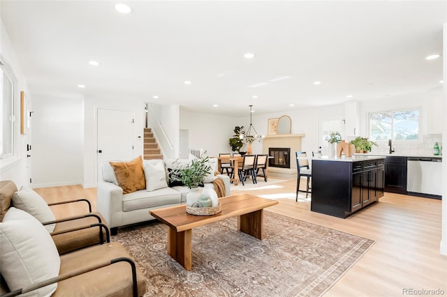 living room featuring light wood-type flooring, stairway, a glass covered fireplace, and recessed lighting