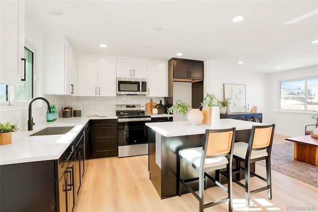 kitchen with decorative backsplash, appliances with stainless steel finishes, light countertops, a kitchen bar, and a sink