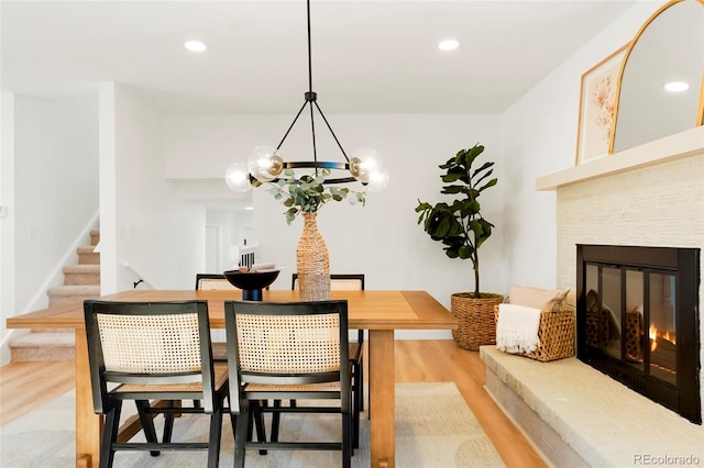 dining room with recessed lighting, light wood-style flooring, stairs, and a tile fireplace