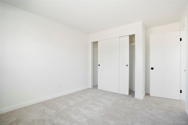 unfurnished bedroom with a closet, light colored carpet, and baseboards