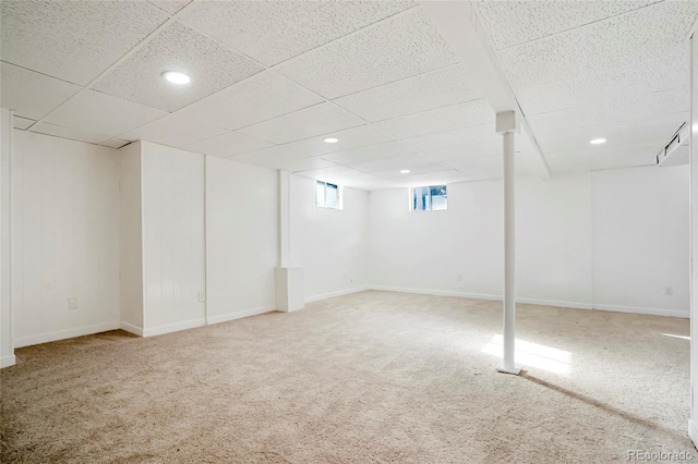 basement featuring baseboards, a drop ceiling, and carpet flooring