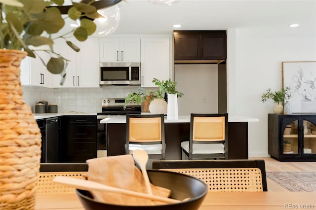 kitchen with decorative backsplash, light countertops, light wood-style floors, appliances with stainless steel finishes, and white cabinetry