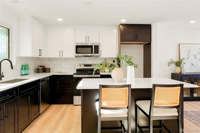 kitchen with a sink, white cabinetry, stainless steel appliances, light wood finished floors, and light countertops