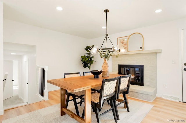 dining room featuring light wood-type flooring, recessed lighting, baseboards, a brick fireplace, and a chandelier
