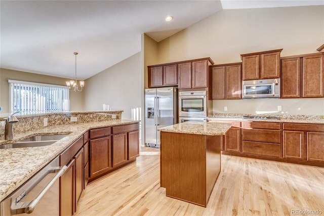 kitchen with a kitchen island, stainless steel appliances, sink, hanging light fixtures, and light hardwood / wood-style flooring