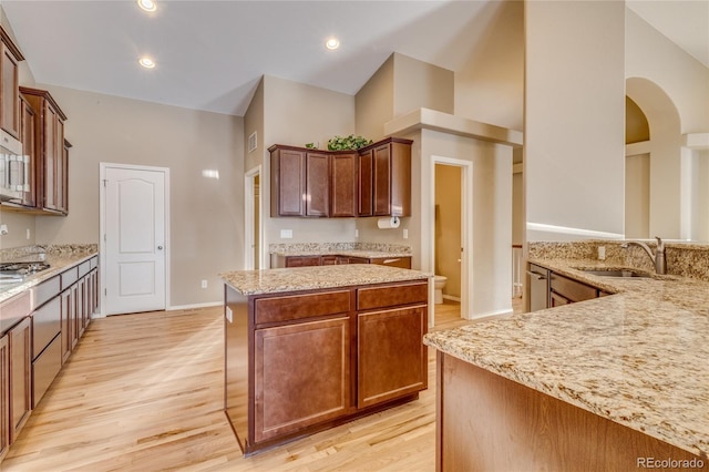 kitchen with light stone countertops, a high ceiling, a center island, light hardwood / wood-style floors, and sink