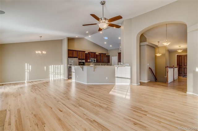 unfurnished living room featuring ceiling fan with notable chandelier, light hardwood / wood-style floors, and high vaulted ceiling