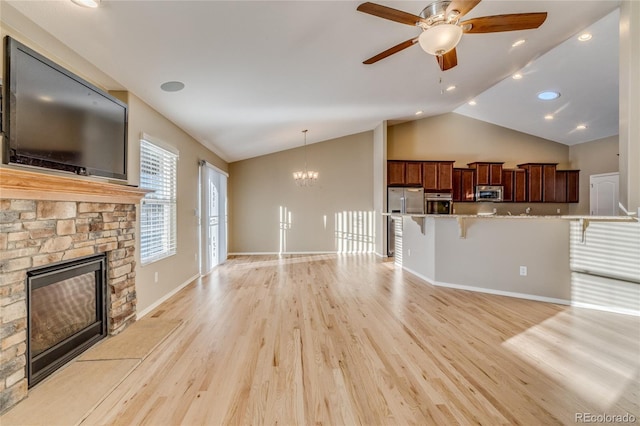 unfurnished living room featuring vaulted ceiling, a stone fireplace, ceiling fan with notable chandelier, and light hardwood / wood-style flooring