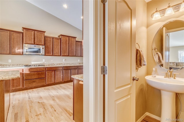 kitchen featuring light stone countertops, stainless steel appliances, light hardwood / wood-style flooring, and vaulted ceiling