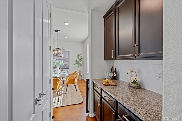 kitchen with decorative backsplash, light wood-type flooring, light stone counters, dark brown cabinets, and a chandelier