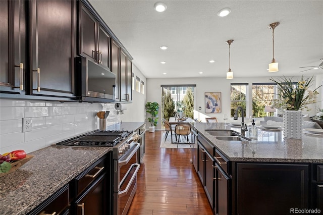 kitchen featuring sink, hanging light fixtures, stainless steel appliances, dark hardwood / wood-style floors, and an island with sink