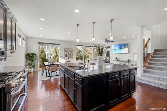 kitchen with a kitchen island with sink, dark hardwood / wood-style flooring, dark stone counters, and appliances with stainless steel finishes