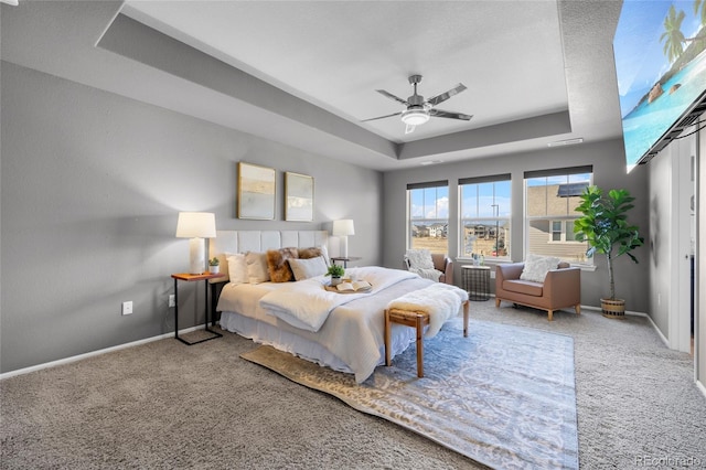 carpeted bedroom with ceiling fan and a raised ceiling