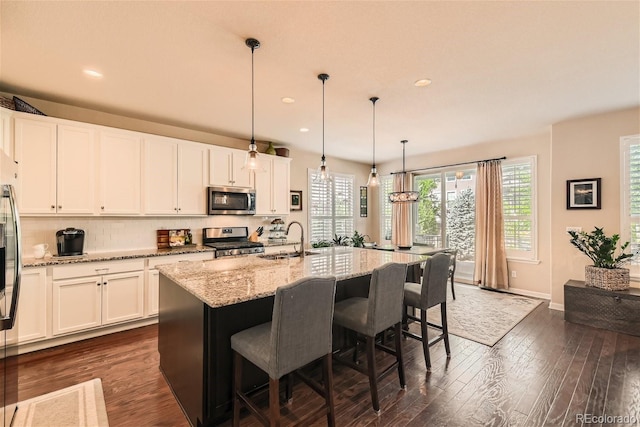 kitchen featuring stainless steel appliances, a sink, white cabinets, backsplash, and dark wood finished floors