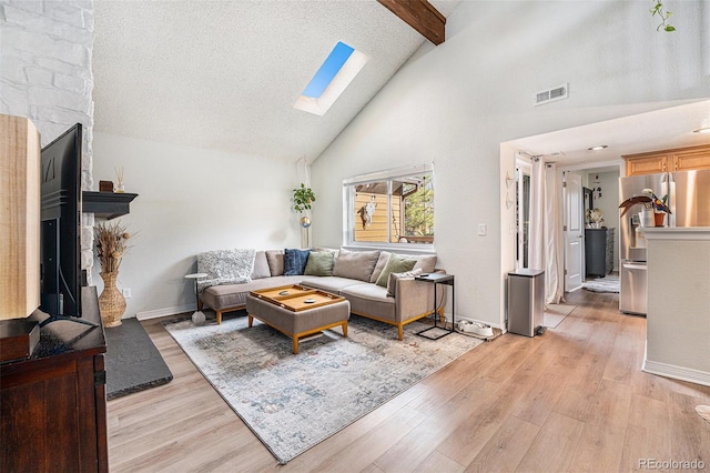 living room featuring visible vents, beamed ceiling, high vaulted ceiling, light wood-style flooring, and a skylight