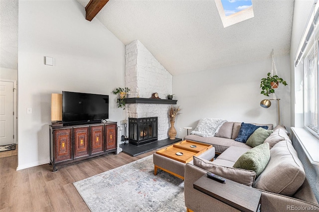 living area featuring beam ceiling, a stone fireplace, a textured ceiling, and wood finished floors