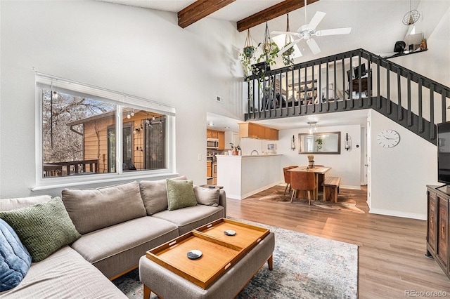 living room featuring light wood finished floors, baseboards, beamed ceiling, stairs, and a ceiling fan