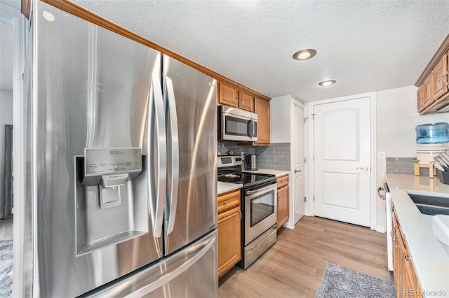 kitchen featuring light wood-type flooring, stainless steel appliances, brown cabinets, and backsplash