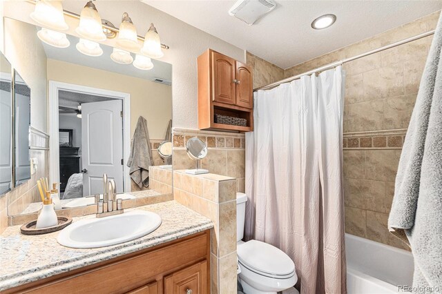 bathroom featuring vanity, visible vents, shower / bath combo, tile walls, and toilet