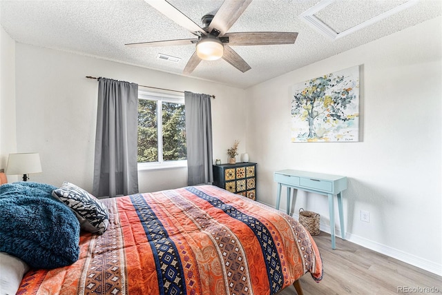 bedroom featuring wood finished floors, baseboards, visible vents, attic access, and a textured ceiling