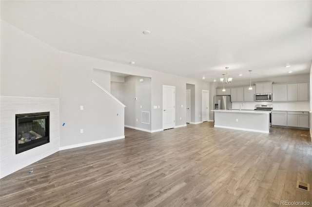 14249 Beebalm Ave, Parker, CO 80134 - unfurnished living room featuring baseboards, wood finished floors, a tiled fireplace, a sink, and recessed lighting