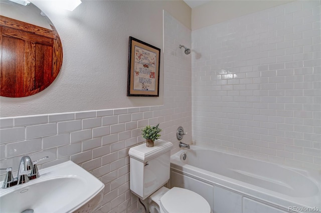 full bathroom featuring tile walls, sink, tiled shower / bath combo, and toilet