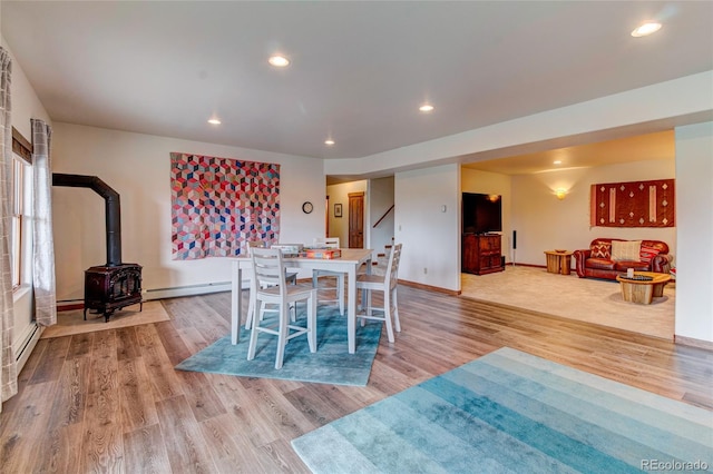 dining space with light hardwood / wood-style flooring, baseboard heating, and a wood stove