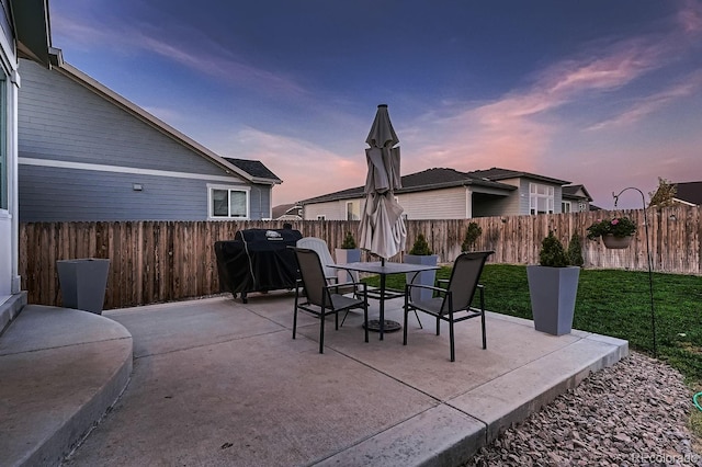 patio terrace at dusk featuring a lawn and area for grilling