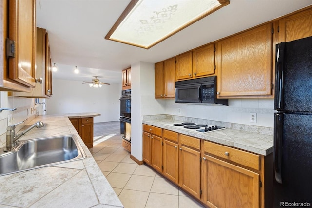 kitchen with sink, ceiling fan, black appliances, light tile patterned flooring, and tile countertops