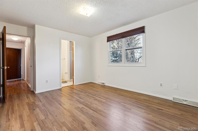 unfurnished bedroom with connected bathroom, a textured ceiling, and light wood-type flooring