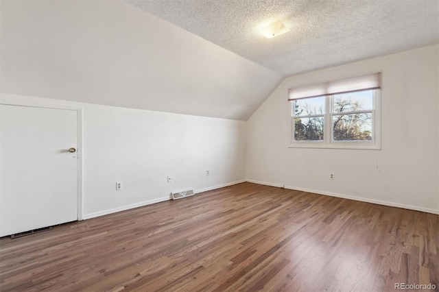 additional living space with lofted ceiling, hardwood / wood-style flooring, and a textured ceiling