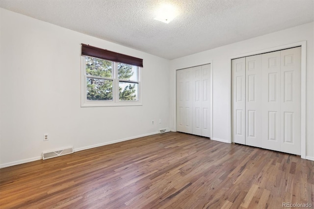 unfurnished bedroom with multiple closets, wood-type flooring, and a textured ceiling