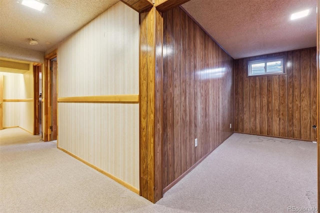 hall with wood walls, light carpet, and a textured ceiling