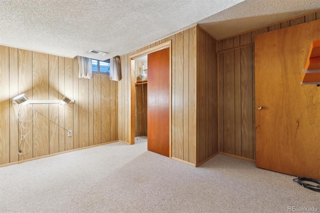 interior space featuring light colored carpet, a textured ceiling, and wooden walls